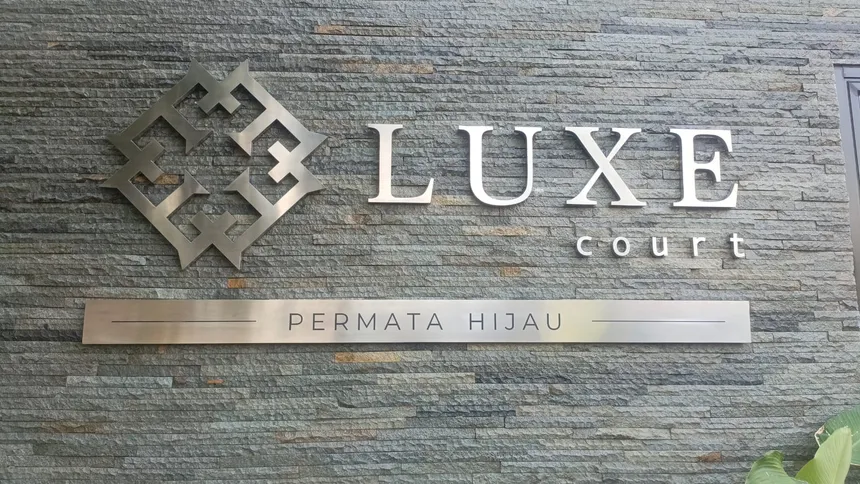 Huruf timbul stainless bertuliskan LUXE court terpasang pada dinding batu alam