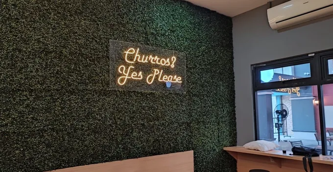 Tulisan neon flex tipis pada dinding tanaman di area kafe