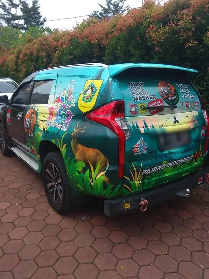 Bagian belakang SUV dengan wrap penuh bergambar rusa dan lanskap wisata